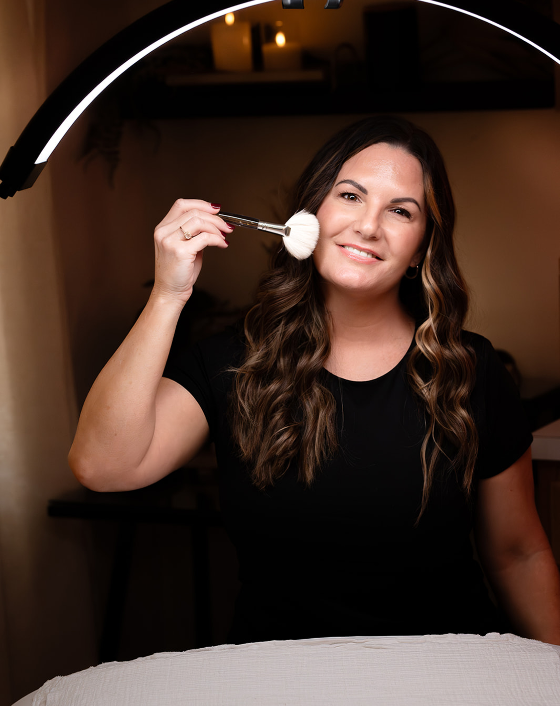 Woman holding a makeup brush with a lighted mirror in the background